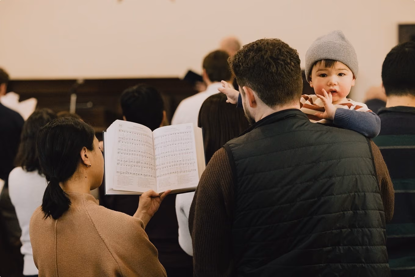 Congregation singing from psalters during worship, a child looking on