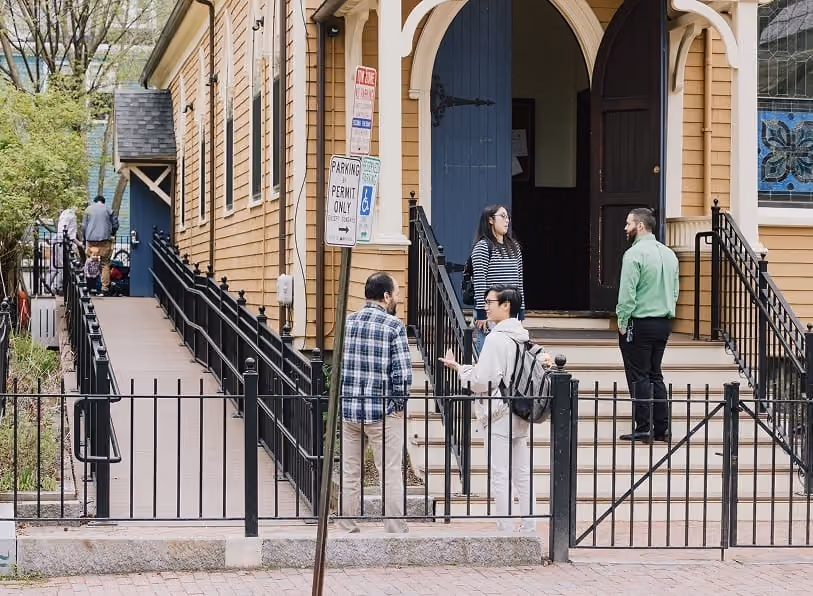Exterior of the church meeting house with members gathered on the steps