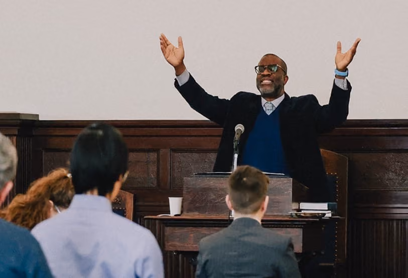 Man preaching from the pulpit with hands raised during worship